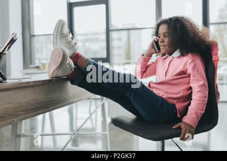 Poco americano africano imprenditrice con le gambe sul tavolo utilizzando lo smartphone nel ufficio moderno Foto Stock