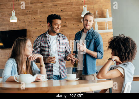 Due uomini sono diffidenti nei confronti delle giovani donne in seduta cafe Foto Stock