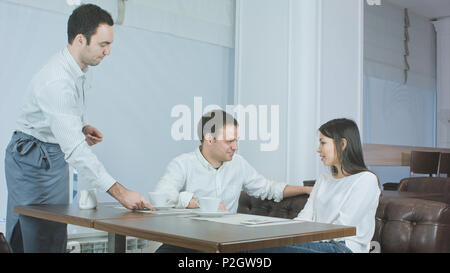 Felice coppia giovane chiacchierando in cafe mentre il cameriere portando caffè o tè Foto Stock