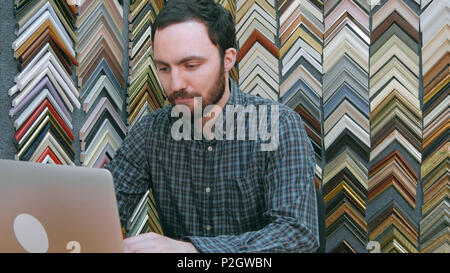 Ritratto di un giovane maschio titolare di azienda lavorano su laptop dietro il bancone del suo negozio Foto Stock