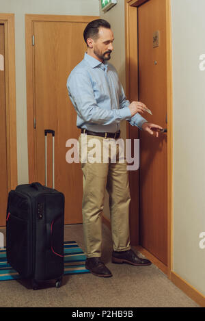 Uomo Barbuto con la valigia tenendo la scheda e apertura sportello hotel Foto Stock