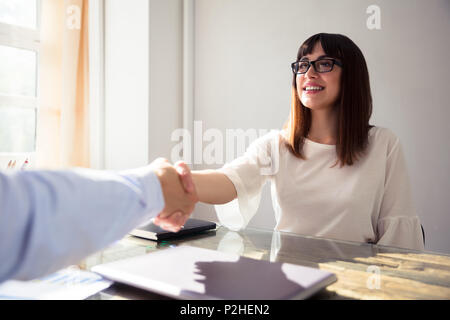 Felice giovane imprenditrice agitando la mano con il suo collega sulla scrivania Foto Stock