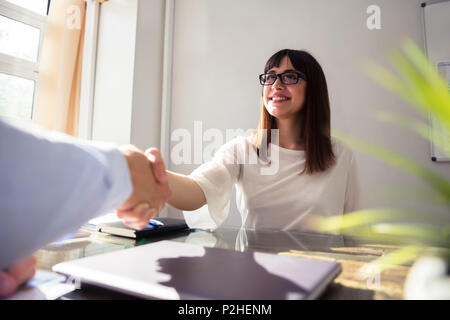 Felice giovane imprenditrice agitando la mano con il suo collega sulla scrivania Foto Stock