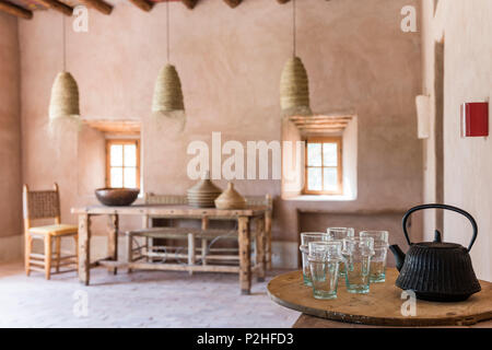 Ghisa teiera e bicchieri in primo piano del marocchino sala da pranzo con il rattan oendant luci, terra di pareti e pavimenti in terracotta Foto Stock
