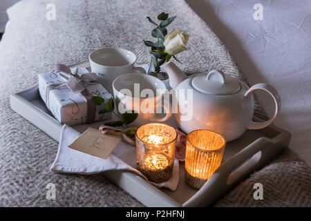 Dettaglio di una delle tealight accesa prima colazione vassoio con piccoli avvolti presente e rosa bianca. Foto Stock