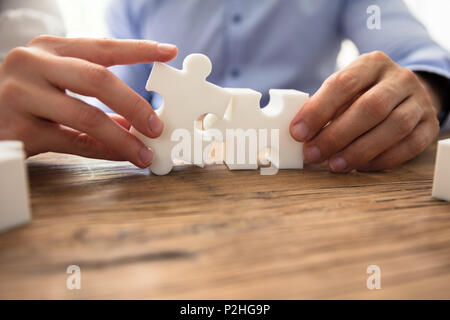 Close-up di due imprenditori White Jigsaw pezzi su scrivania in legno Foto Stock