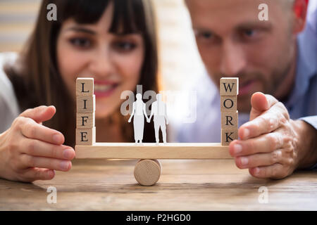 Coppia felice la protezione di equilibrio tra lavoro e vita familiare e carta ritagliata su altalena Foto Stock