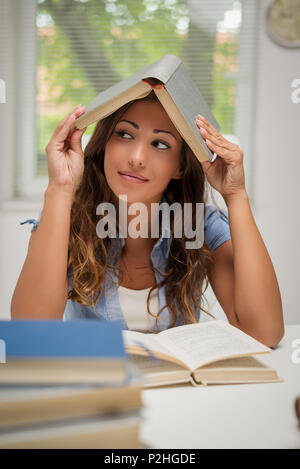 Bella annoiato giovane donna apprendimento nella libreria. Lei si diverte con un libro sopra la sua testa. Foto Stock