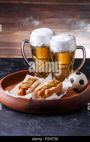 Immagine di due bicchieri di birra, hot dogs, pallone da calcio Foto Stock