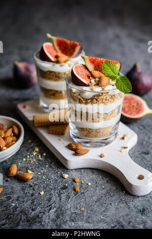 Layered dessert mascarpone con frantumato biscotti alla vaniglia, i fichi e le mandorle in un vasetto di vetro Foto Stock