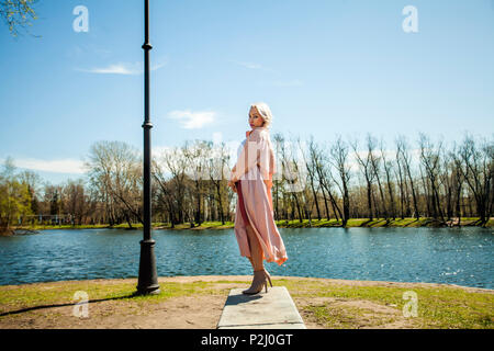 Moda Donna in rosa setoso cappotto e stivaletti, Street Fashion ritratto all'aperto Foto Stock