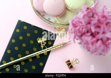 Rosa luminoso giacinto con French macarons, una tazza di caffè e gold nero cartoleria.femminile business lifestyle & Lavoro da casa concetto. La molla del tema. Foto Stock