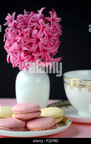 Rosa luminoso giacinto con French macarons, una tazza di caffè e gold nero cartoleria.femminile business lifestyle & Lavoro da casa concetto. La molla del tema. Foto Stock