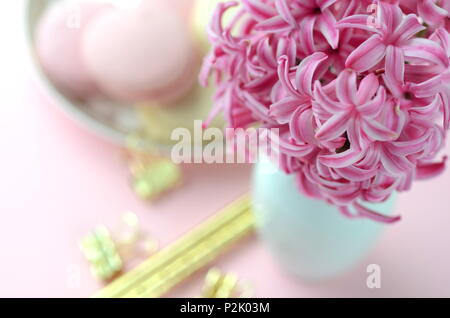 Rosa luminoso giacinto con French macarons, una tazza di caffè e gold nero cartoleria.femminile business lifestyle & Lavoro da casa concetto. La molla del tema. Foto Stock