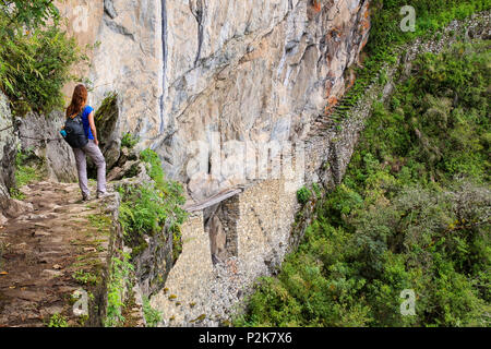 Giovane donna godendo la vista del Ponte di Inca e cliff percorso nei pressi di Machu Picchu in Perù. Il ponte è una parte di un sentiero di montagna che capi ad ovest di M Foto Stock