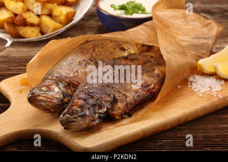 Sfornato fresco pesce avvolto in carta con patate e dip bianco su sfondo di legno Foto Stock