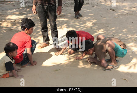 Due ragazzi cambogiano giocando a un gioco di marmi con piccole sfere di vetro sulla ruvida massa sabbiosa della risma scuola parco giochi. Foto Stock