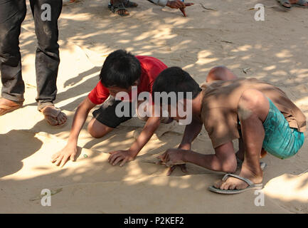 Due ragazzi cambogiani il gioco dei marmi, con piccole sfere di vetro, sulla ruvida terra sabbiosa della risma scuola parco giochi. Foto Stock