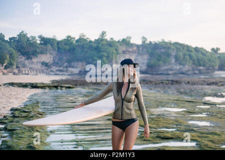 Giovane donna in wetsuit a piedi dalla riva del mare con la tavola da surf in sera Foto Stock