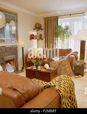 Plaid di lana su divani in pelle marrone a townhouse soggiorno con caminetto a gas e una cassa di legno usato come tavolino da caffè Foto Stock