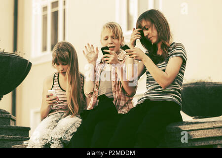 Un gruppo di ragazze adolescenti chiamata sui telefoni cellulari contro un edificio scolastico Foto Stock