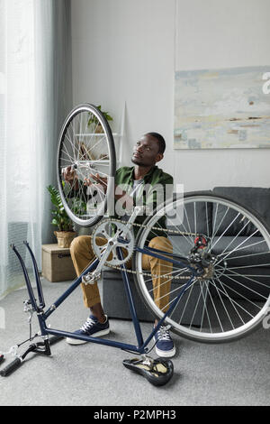 Bello afro uomo controllando la ruota di bicicletta a casa Foto Stock