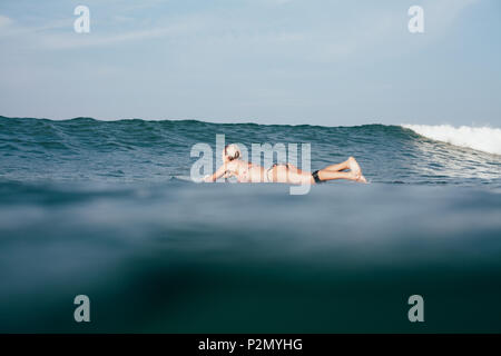 Giovane donna in bikini nuoto sulla tavola da surf Foto Stock