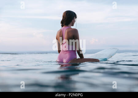 Vista posteriore di giovani sportive seduto sulla tavola da surf in acqua Foto Stock