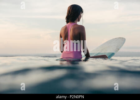 Vista posteriore di sportive seduto sulla tavola da surf in acqua nell'oceano al tramonto Foto Stock