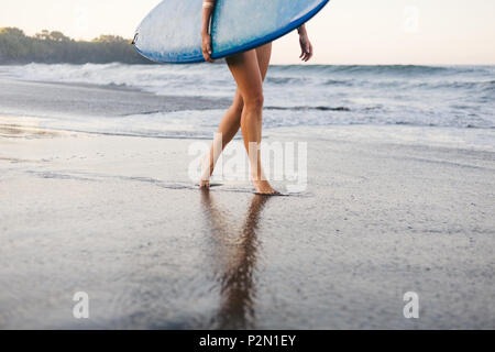 Ritagliato colpo di sportive in costume da bagno con blue surf board camminando sul litorale Foto Stock