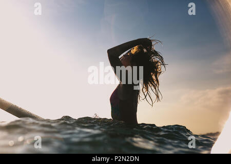 Silhouette di donna ritoccato i capelli mentre è seduto sulla scheda di navigazione in oceano Foto Stock