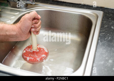 Uomo con uno stantuffo con una mano e acqua nel lavello, utilizzati per pulire un ostruito / bloccato lavello da cucina Foto Stock