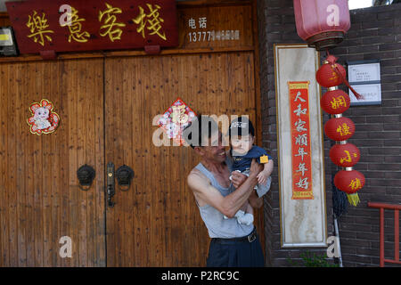 (180616) -- NINGBO, Giugno 16, 2018 (Xinhua) -- un turista porta il suo nipote in armi di fronte in una locanda di Sanshan villaggio del distretto Beilun in Ningbo, Cina orientale della provincia di Zhejiang, 14 giugno 2018. Trasformata da un villaggio di pescatori, Beilun sta diventando un costiere area urbana con la porta dell'industria. Ningbo lo Sviluppo Economico e Tecnologico della Zona di Ningbo, zona di libero commercio, Ningbo Daxie per lo sviluppo della zona, Ningbo Export Processing Zone e Ningbo Meishan area saldata si trovano in Beilun. Il cargo throughput di Ningbo Port Zhoushan, con Beilun porta come la sua anima, ha classificato al primo in un continuo Foto Stock