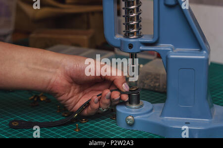 Tanner mette dei rivetti sul cinturino in pelle. Close-up foto. Processo di lavorazione in officina. Foto Stock