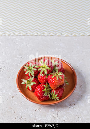 Fragole appena raccolte in una piccola ciotola in bright tavolo rustico Foto Stock