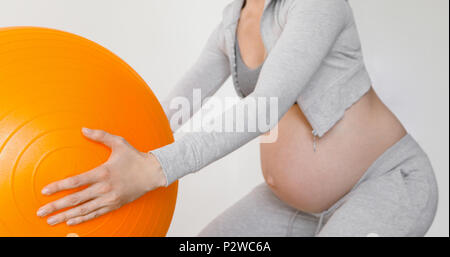 Donna incinta esercitando con montare la sfera facendo squat Foto Stock