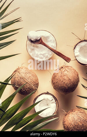 Olio di noce di cocco e noci di cocco su uno sfondo con foglie tropicali. Foto Stock