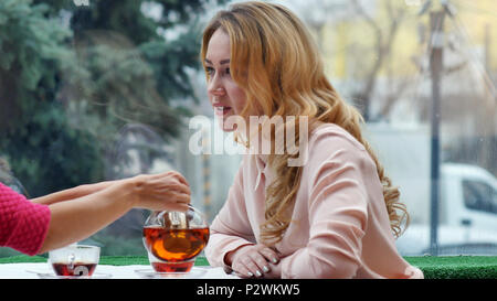 Blonde gustando il tè caldo e parla con un amico in cafe Foto Stock