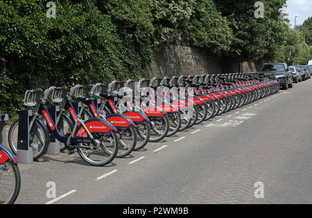 Una lunga linea di Santander-branded biciclette a noleggio in una docking station vicino la stazione ferroviaria di Wandsworth Town nel sud-ovest di Londra, Regno Unito Foto Stock