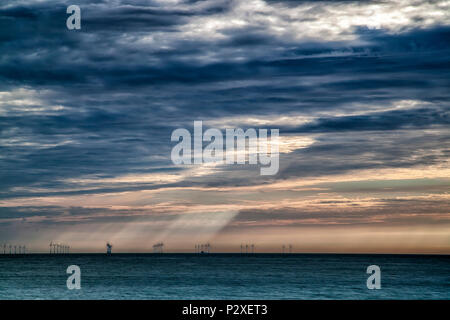 Moody sunrise in mare con albero della luce proveniente attraverso le nuvole e illuminano il lontano le turbine eoliche a Broadstairs Kent, Inghilterra Foto Stock