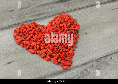 Cumulo di goji berry (wolfberry - Lycium chinense), frutta secca disposte a forma di cuore sul grigio di una tavola di legno. Foto Stock