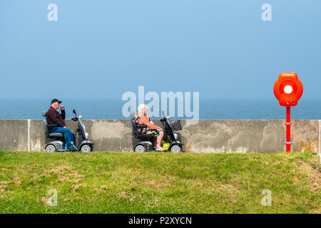 Due persone in mobilità scooter su una passeggiata sulla costa settentrionale del Galles Foto Stock
