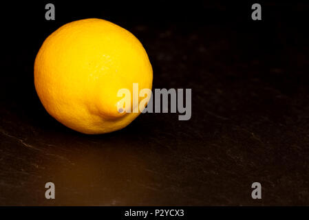 Limone giallo isolato su sfondo scuro su un superficie di ardesia. Frutta mangiare sano concetto Foto Stock
