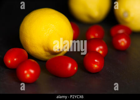Limoni giallo e rosso baby i pomodorini isolata su uno sfondo scuro su un superficie di ardesia. Frutta mangiare sano concetto Foto Stock