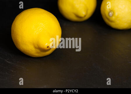 Il giallo dei limoni isolata su uno sfondo scuro su un superficie di ardesia. Frutta mangiare sano concetto Foto Stock