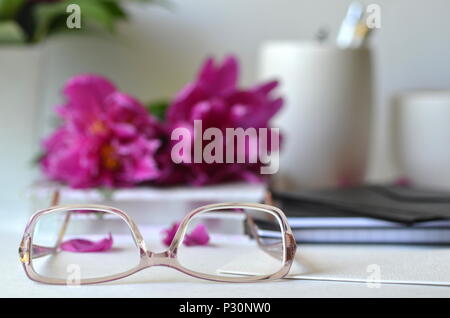 Bold viola peonie rosa con la colorazione rosa bicchieri su una scrivania. Elegante stile femminile area di lavoro desktop. Concetto di lavorare da casa in ufficio, studiare. Foto Stock
