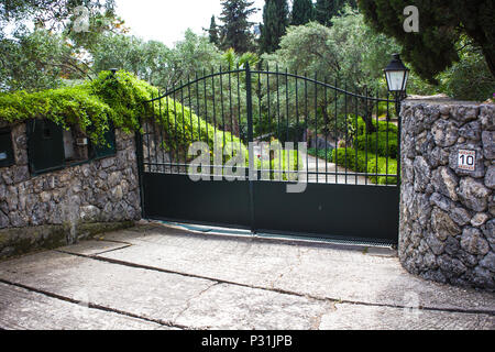 Grande cancello verde andando a un enorme residente. Circondato con diversi tipi di foglie, alberi, fiori nel percorso di andare all'interno dell'edificio. Foto Stock