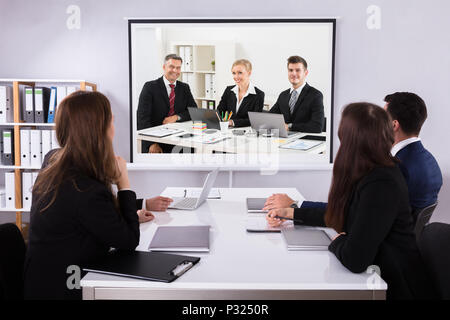 Gruppo di imprenditori alla ricerca di un proiettore con il laptop sulla scrivania in ufficio Foto Stock