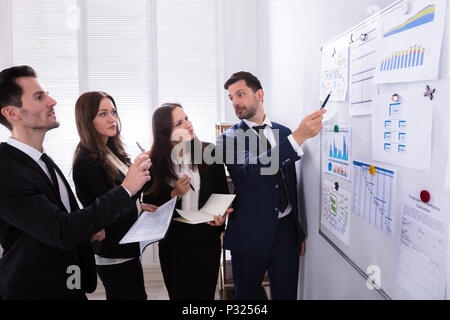 Un gruppo di giovani imprenditori analizzando i grafici sulla scheda bianca al lavoro Foto Stock
