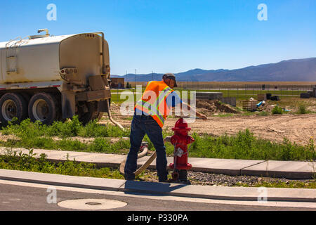 Uomo di ugello di regolazione sull'idrante di fuoco con flessibile collegato nella zona di costruzione. Eagle Mountain, Utah in Utah zona di valle. Foto Stock